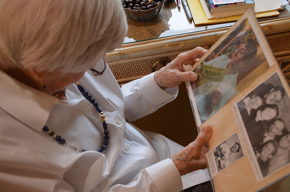 Esther Adler wearing a white shirt sits at her desk in her home in Canton holding a photograph of her family